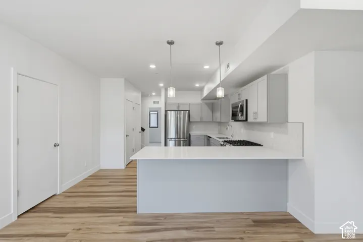 Open-concept kitchen featuring gray cabinetry, stainless steel appliances, white quartz countertops, and a tile backsplash