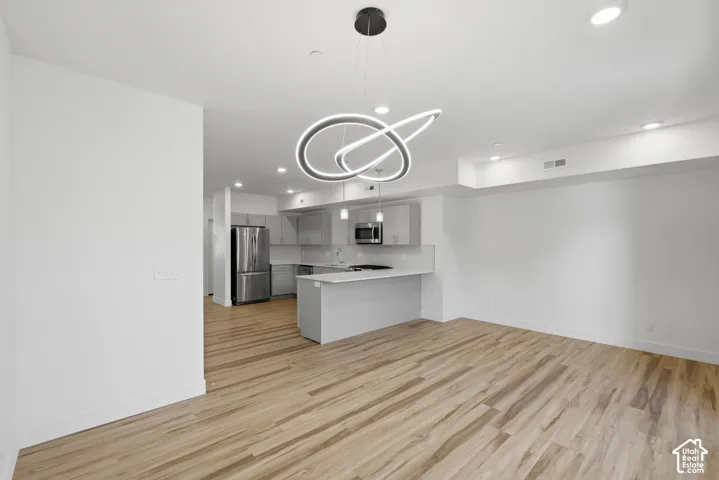 Open-concept living space featuring wood-finish flooring, a modern chandelier, recessed lighting, and a kitchen with stainless steel appliances
