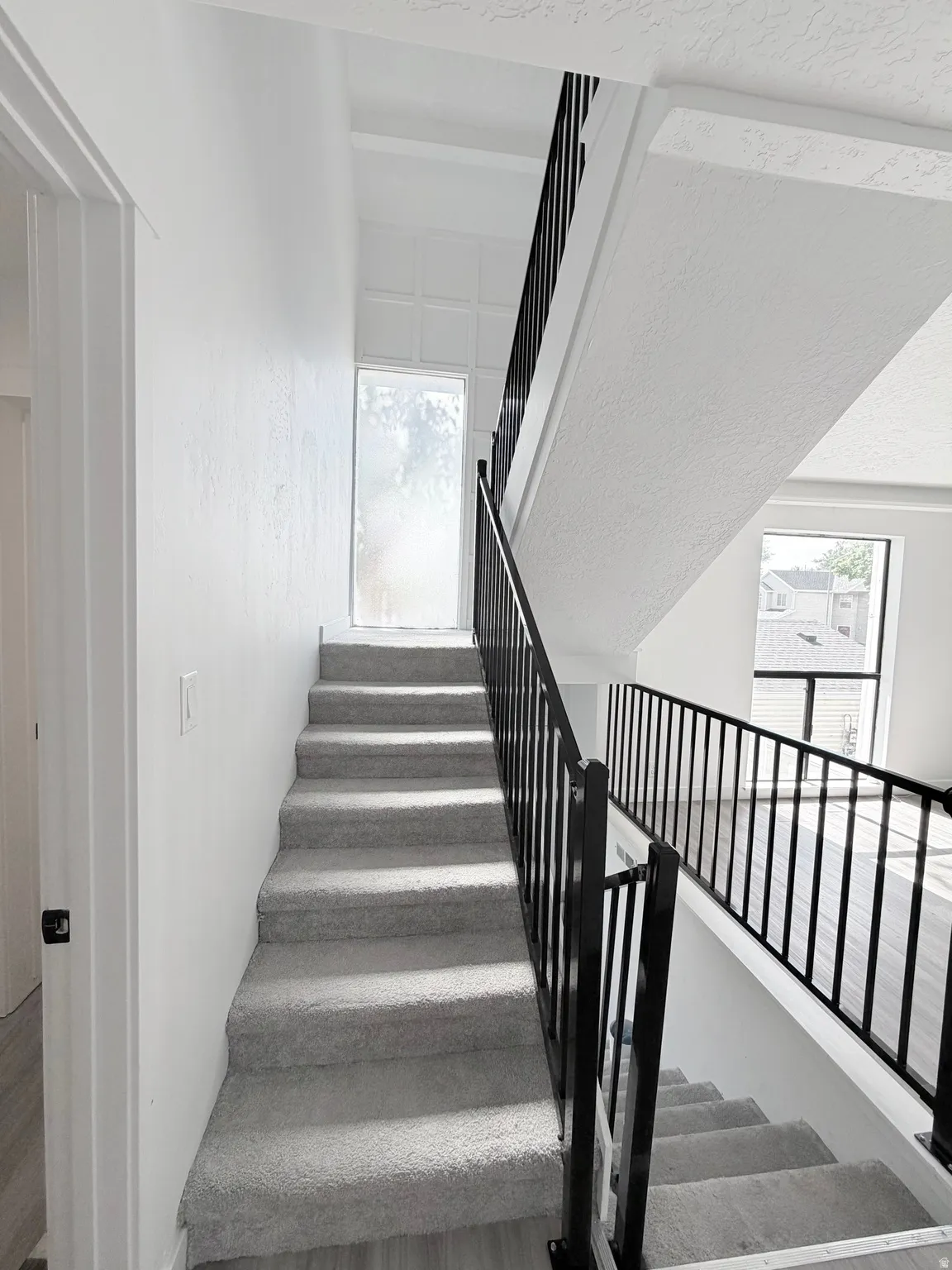 Open-concept staircase featuring light gray carpeting and a contrasting black metal railing