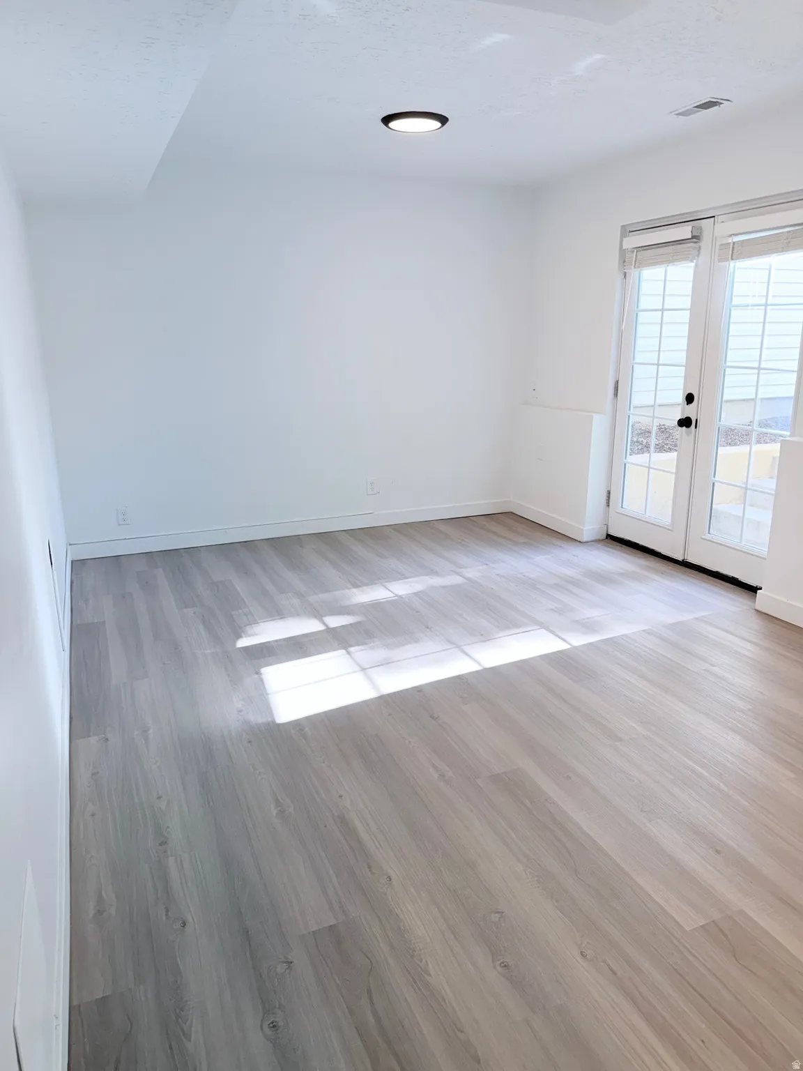 Spacious room with wood-finish flooring, white walls, and a contemporary flush-mount ceiling light