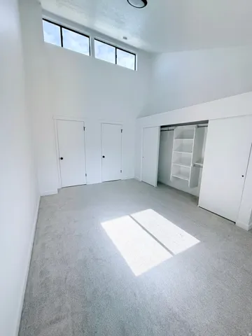 Spacious room featuring a vaulted ceiling with clerestory windows, light gray carpeting, and a built-in closet system with shelving