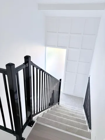 Staircase featuring dark metal railings and light-colored carpeted treads with wood-finish risers