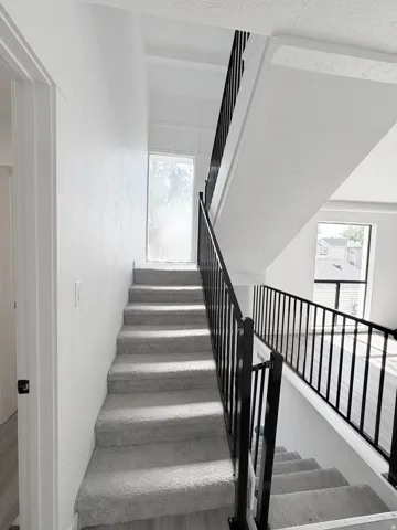 Open-concept staircase featuring light gray carpeting and a contrasting black metal railing