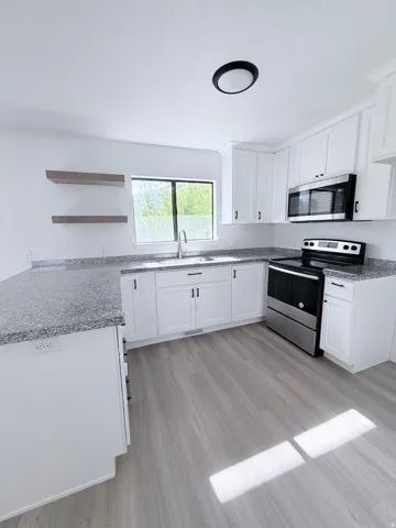 Kitchen featuring white cabinetry, grey speckled countertops, stainless steel appliances, and wood-finish flooring