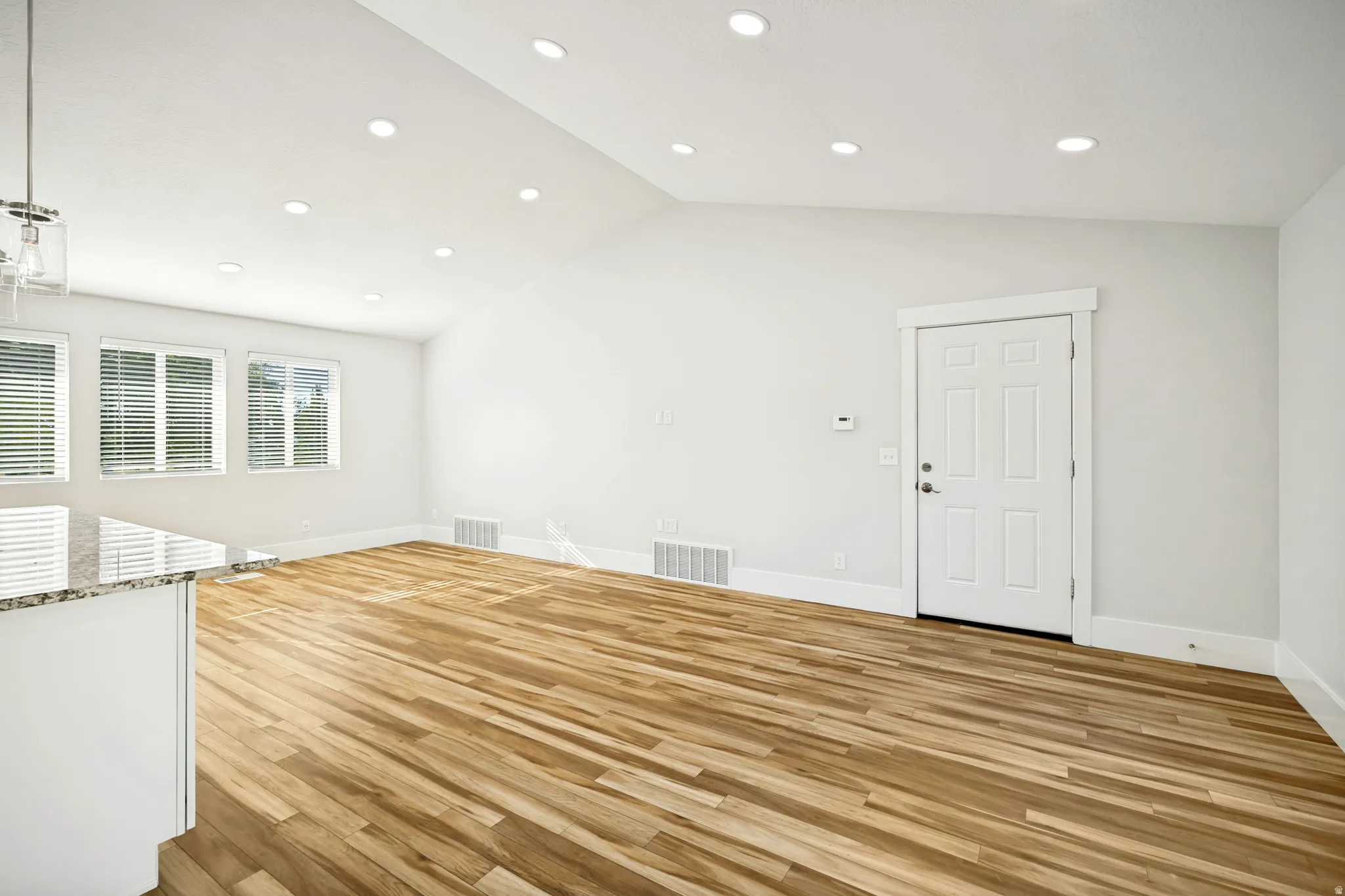 Bright interior space featuring wood-finish flooring, multiple windows with blinds, a white paneled door, and recessed lighting