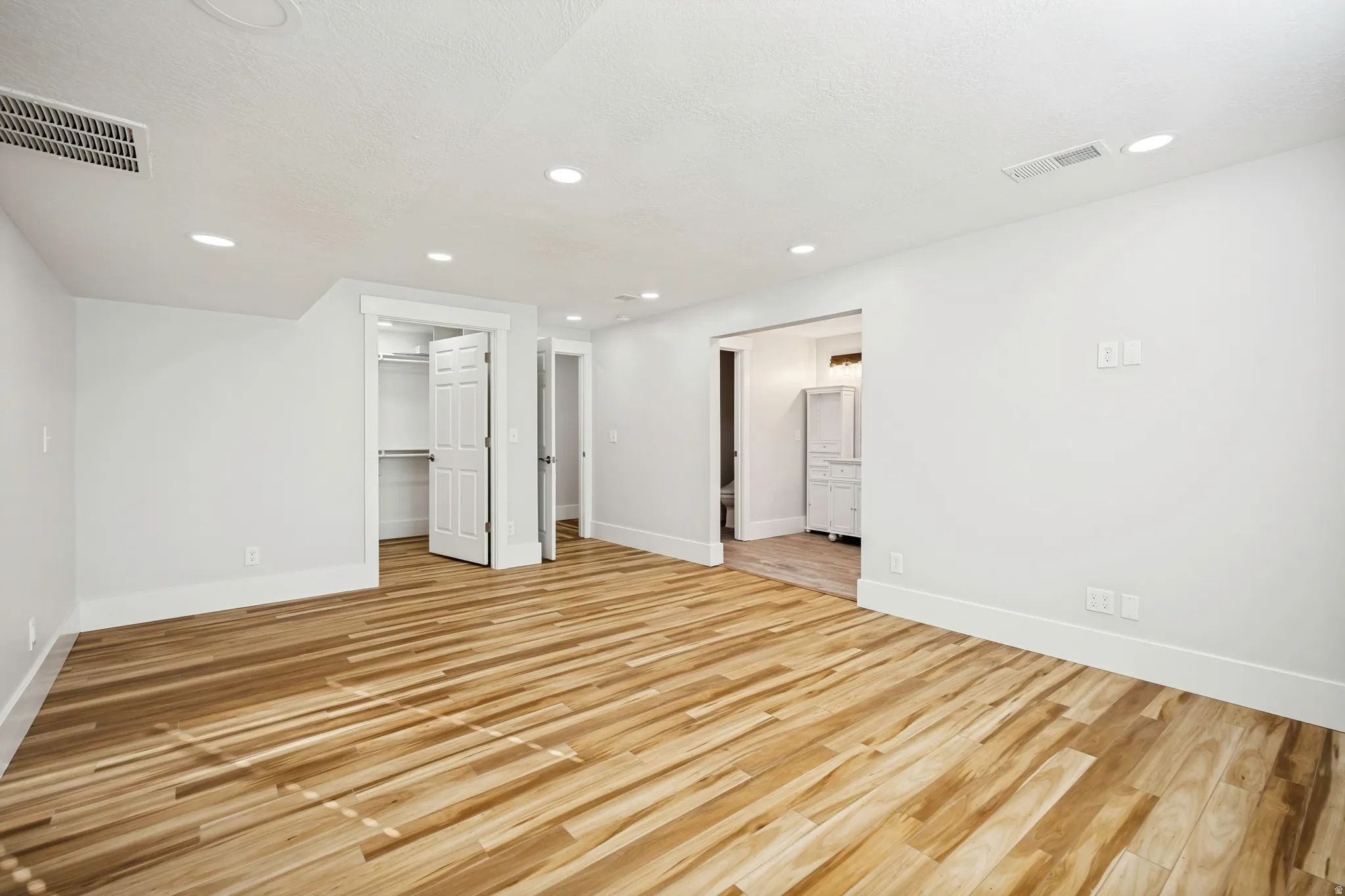 Spacious interior room featuring wood-finish flooring, white walls, and recessed lighting