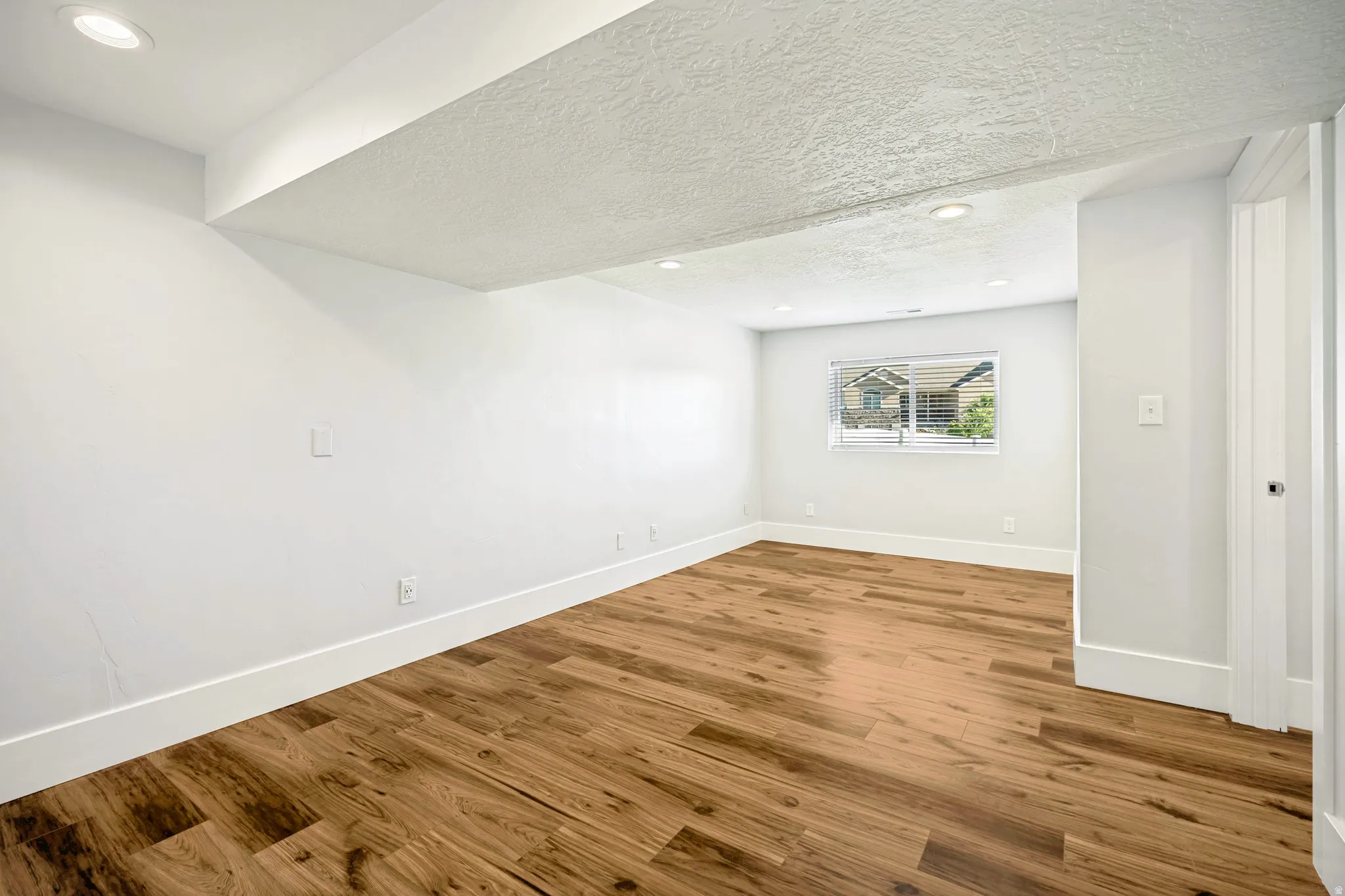 Spacious room featuring wood-finish flooring, recessed lighting, and a window with blinds