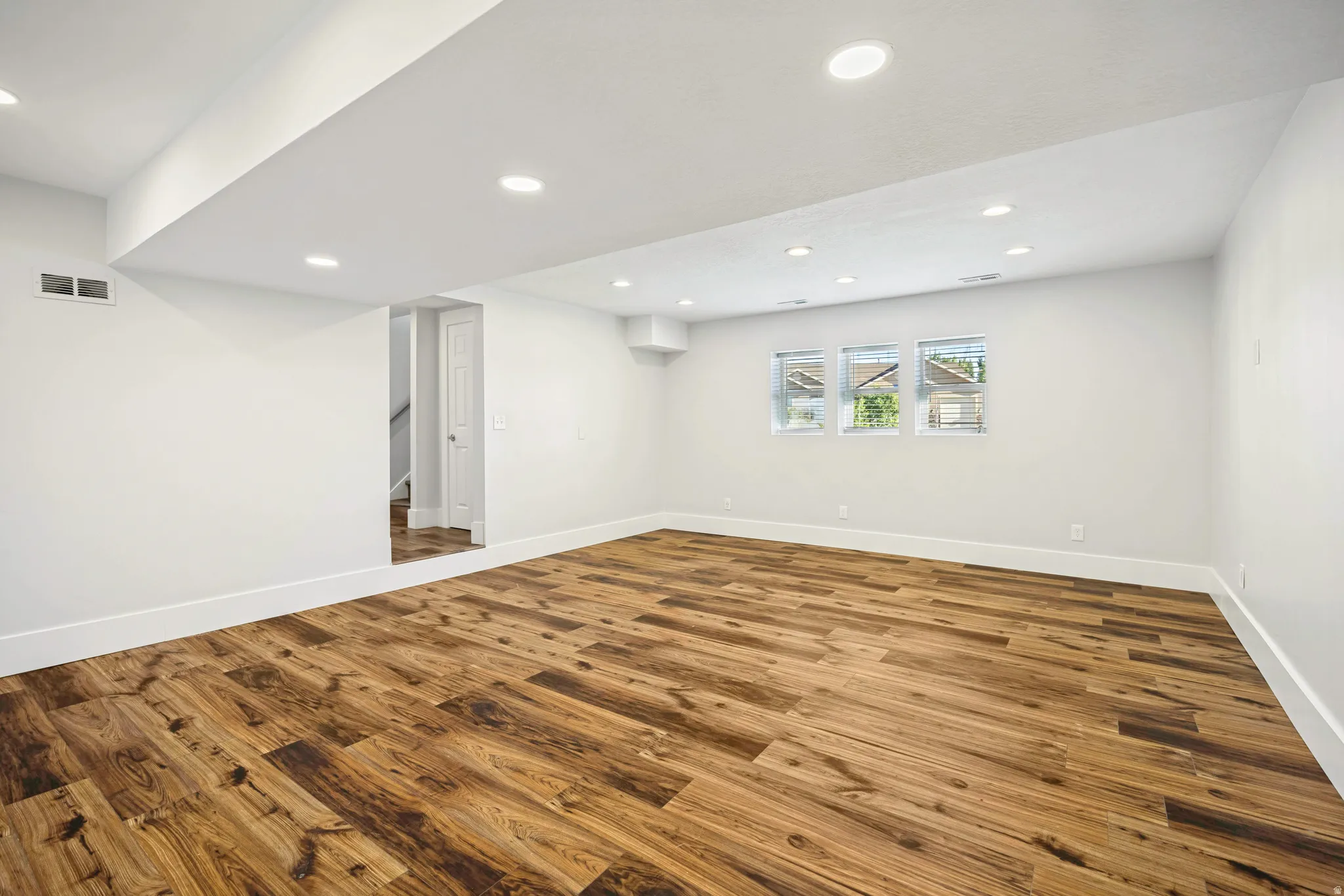 Spacious room featuring wood-finish flooring, white walls, recessed lighting, and three windows