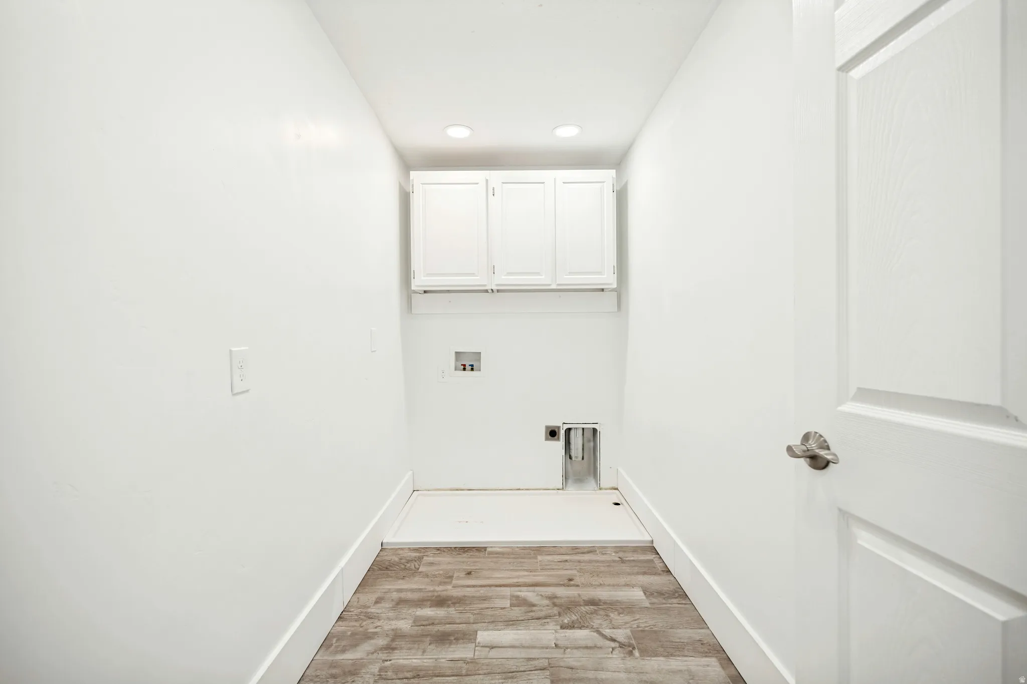 Laundry area featuring wood-finish flooring, white cabinetry, recessed lighting, and a paneled door with brushed nickel hardware