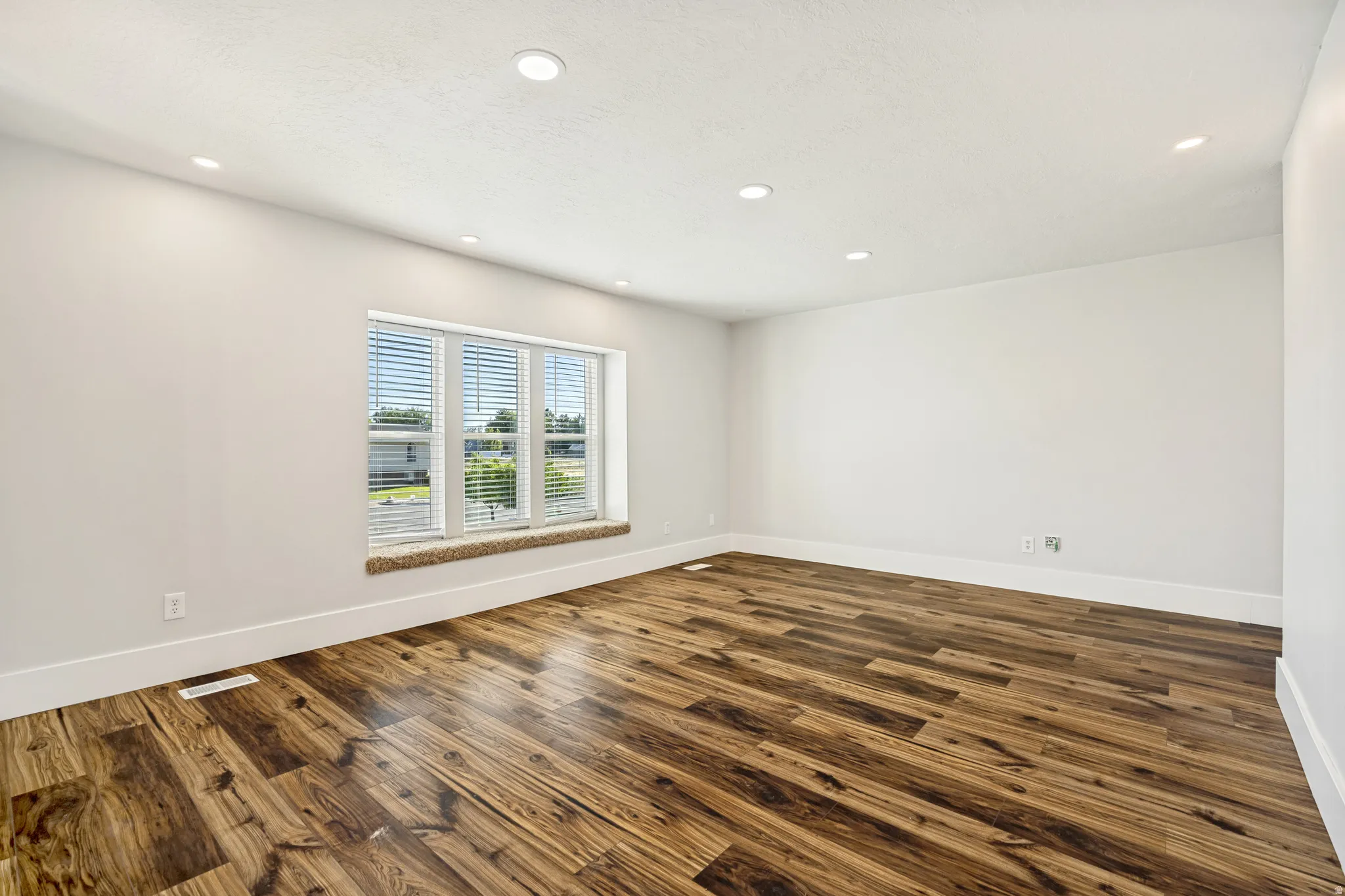 Spacious room featuring wood-finish flooring, recessed lighting, and a large window with blinds