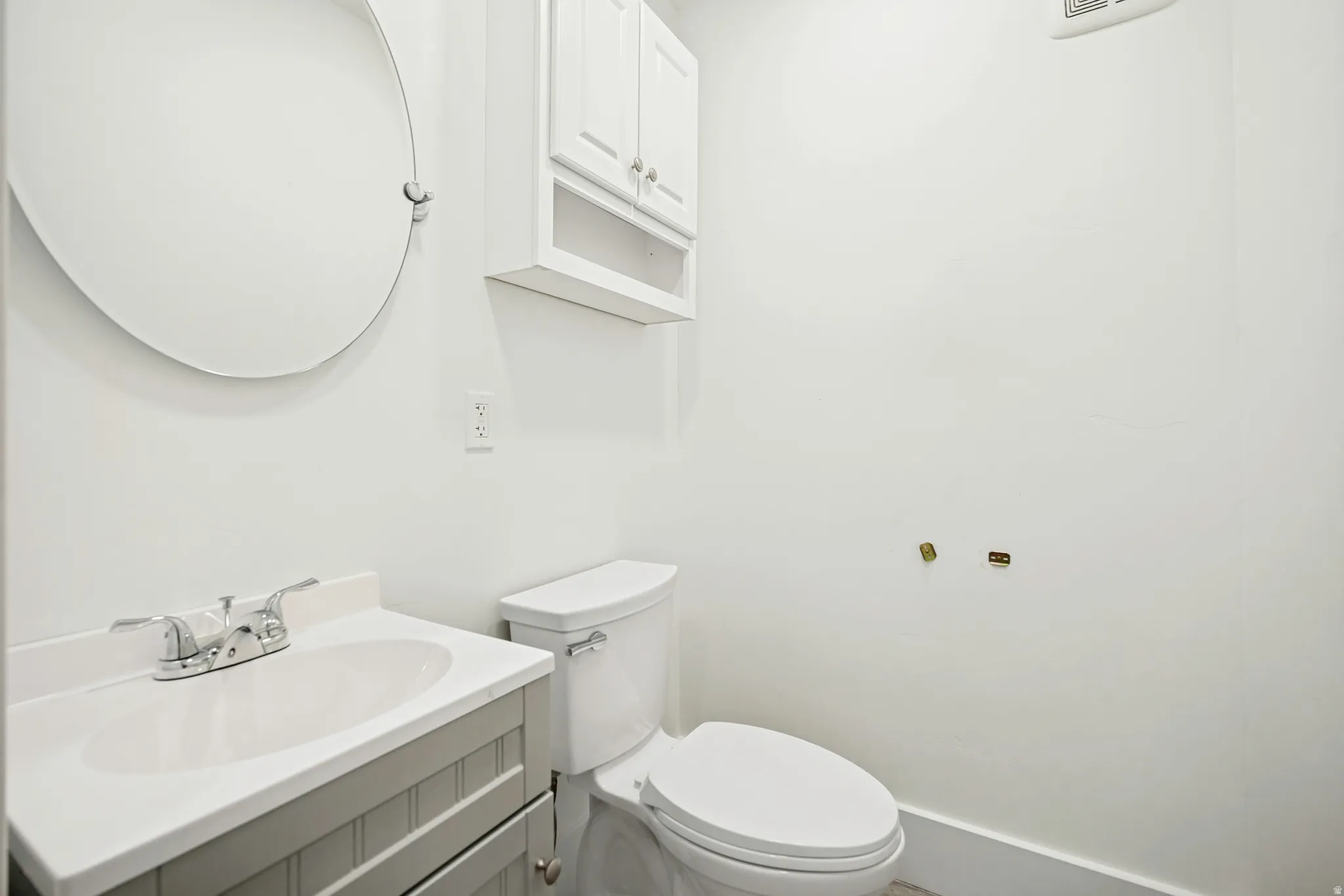 White-painted vanity with integrated sink and chrome faucet, round wall mirror, and white wall cabinet with open shelving