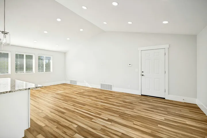 Bright interior space featuring wood-finish flooring, multiple windows with blinds, a white paneled door, and recessed lighting