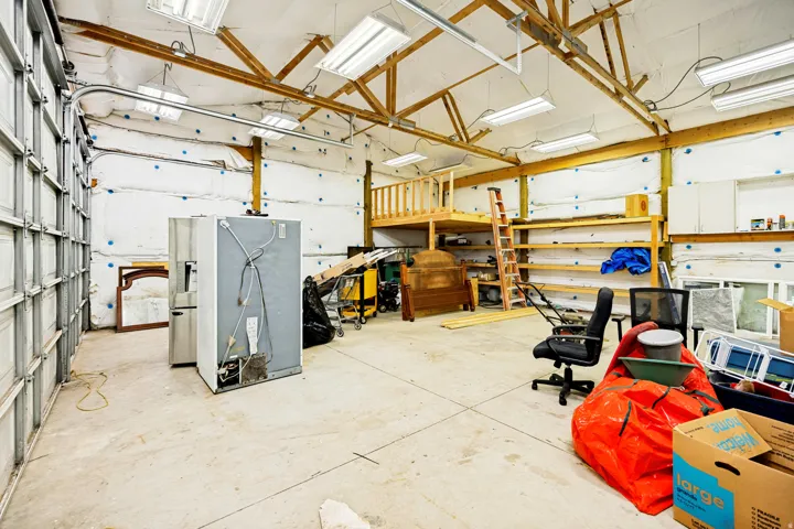 Spacious garage interior featuring high ceilings with exposed wood beams and fluorescent lighting