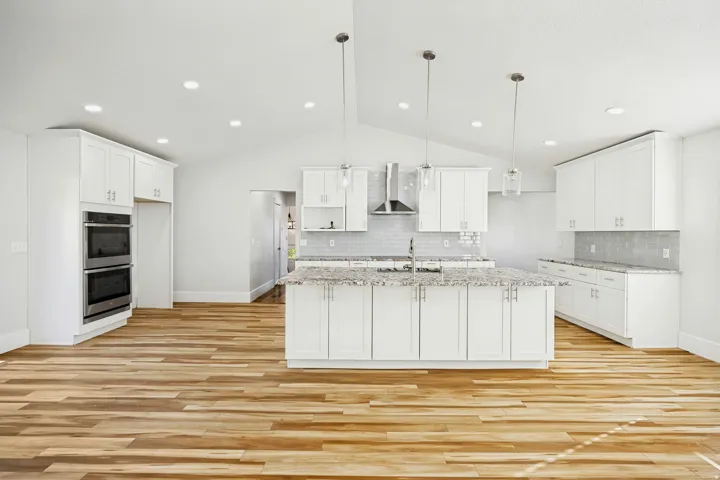 Spacious kitchen featuring an expansive center island with seating, pendant lighting, wood-finish flooring, white cabinetry, and stainless steel double ovens