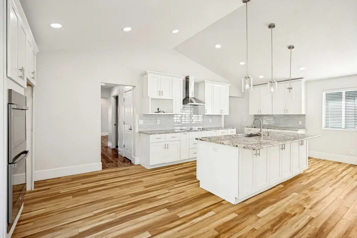 Spacious kitchen featuring an island with a sink, white cabinetry, integrated stainless steel appliances, wood-finish flooring, and recessed lighting