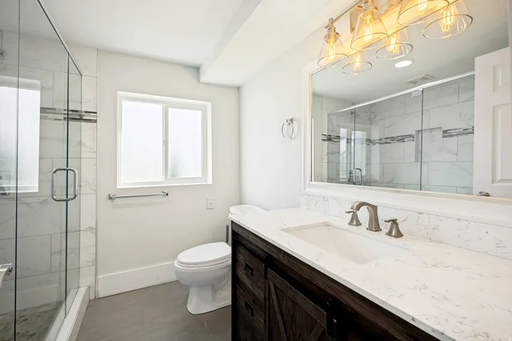 Bathroom featuring a dual-sink vanity with a light-toned countertop, a shower enclosure with glass doors, and a frosted window