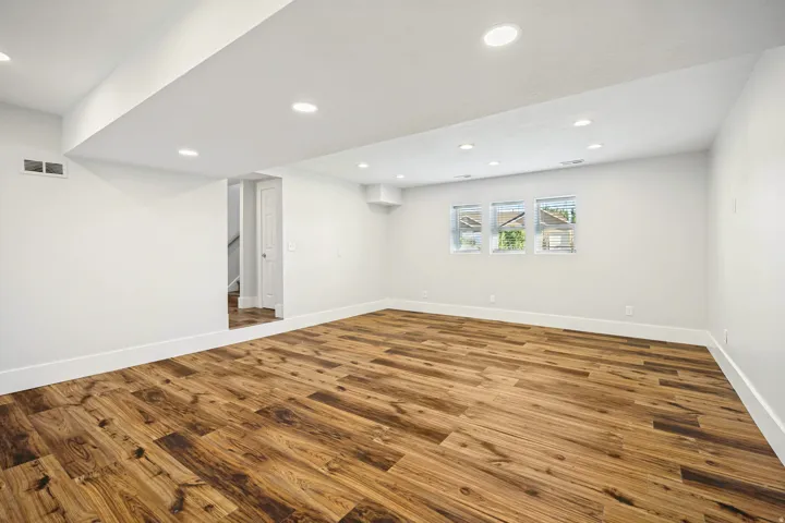 Spacious room featuring wood-finish flooring, white walls, recessed lighting, and three windows