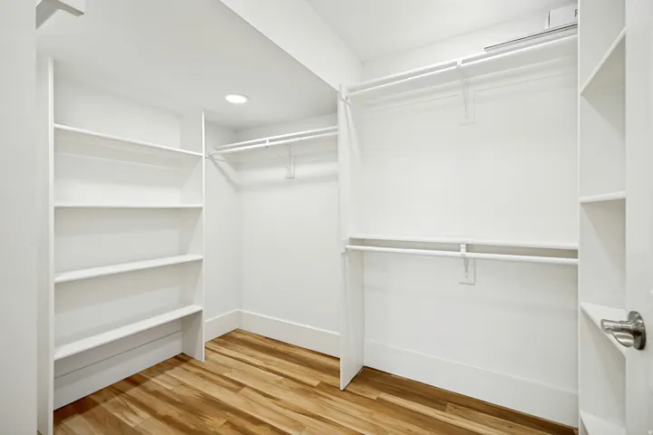 Walk-in closet featuring wood-finish flooring, recessed lighting, white built-in shelving, and white hanging rods