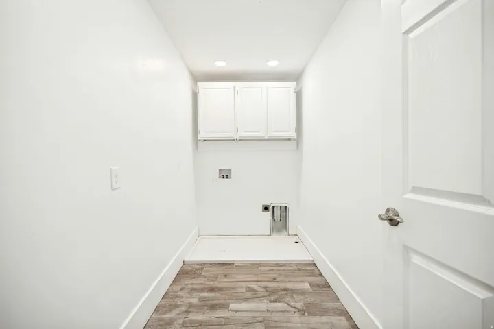 Laundry area featuring wood-finish flooring, white cabinetry, recessed lighting, and a paneled door with brushed nickel hardware