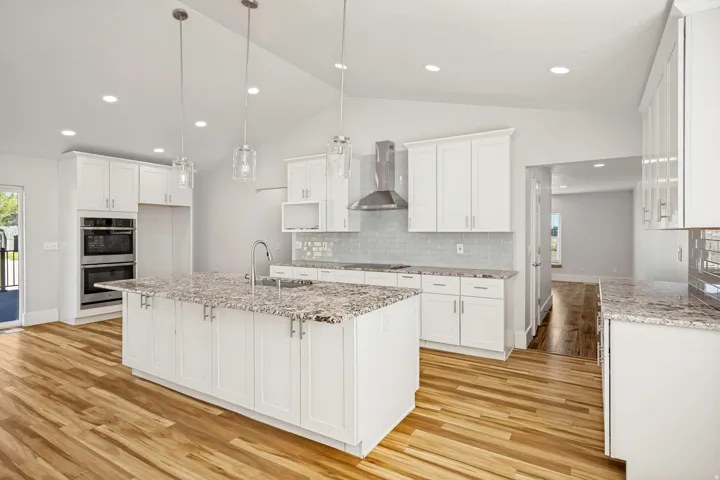 Open-concept kitchen featuring an expansive center island with an undermount sink, granite countertops, white shaker cabinetry, stainless steel double wall ovens, and wood-finish flooring