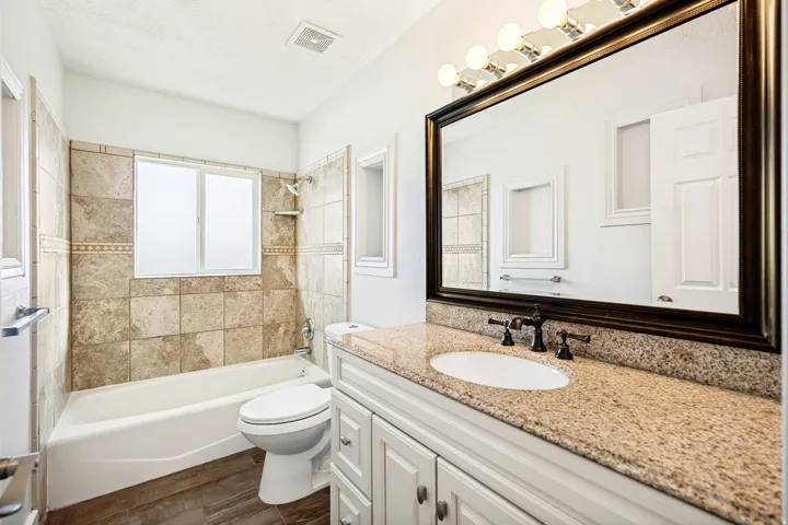Bathroom featuring a built-in tub with tile surround, a single vanity with a solid surface countertop, white cabinetry, and wood-finish flooring