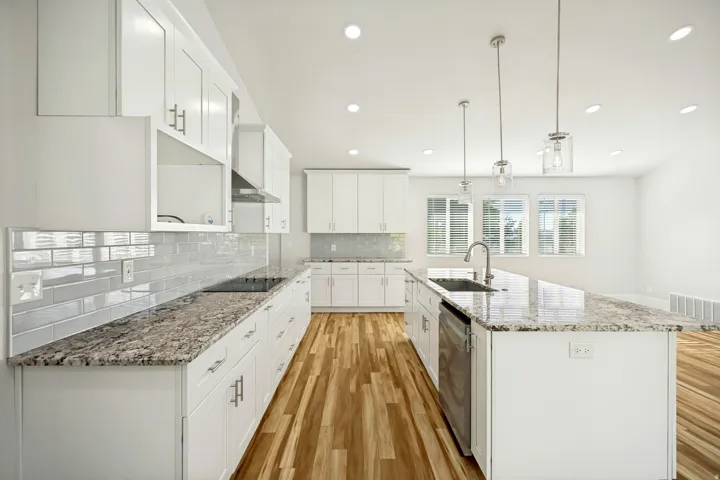 Modern kitchen featuring white cabinetry, a large center island with a stainless steel sink, granite countertops, and wood-finish flooring