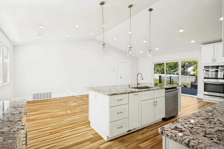 Kitchen featuring an expansive island with granite countertops, stainless steel appliances, and white cabinetry