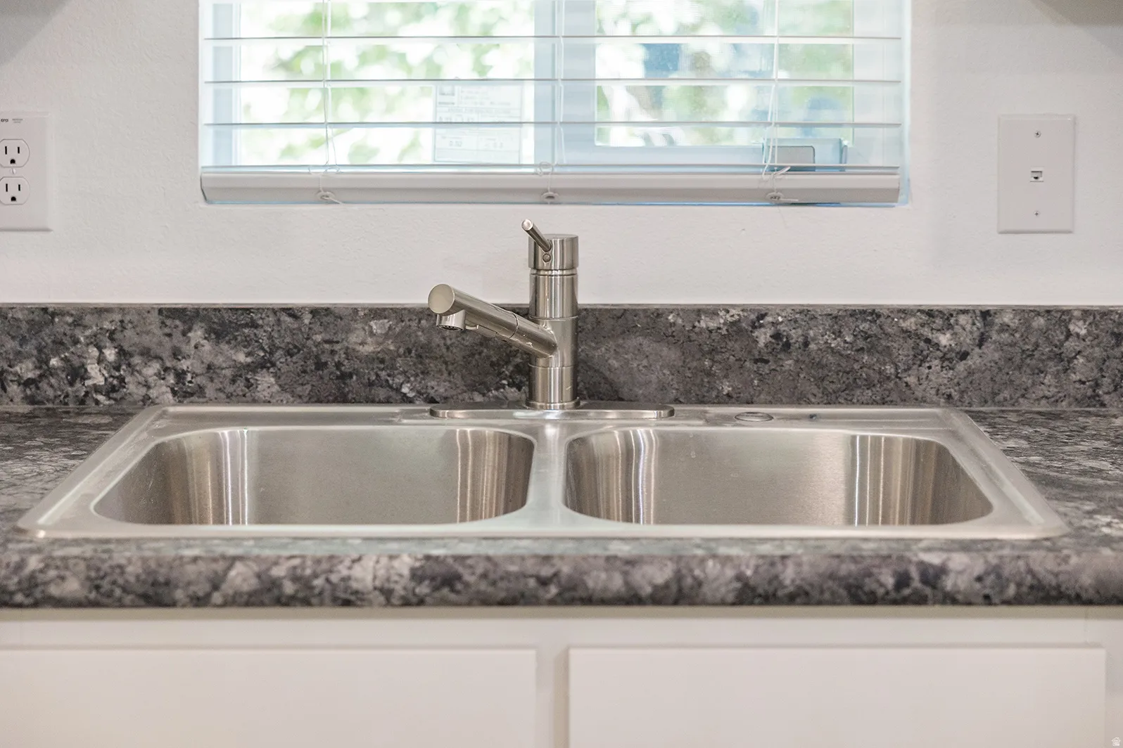 Dual-basin stainless steel sink with a single-handle faucet, set into a dark speckled countertop