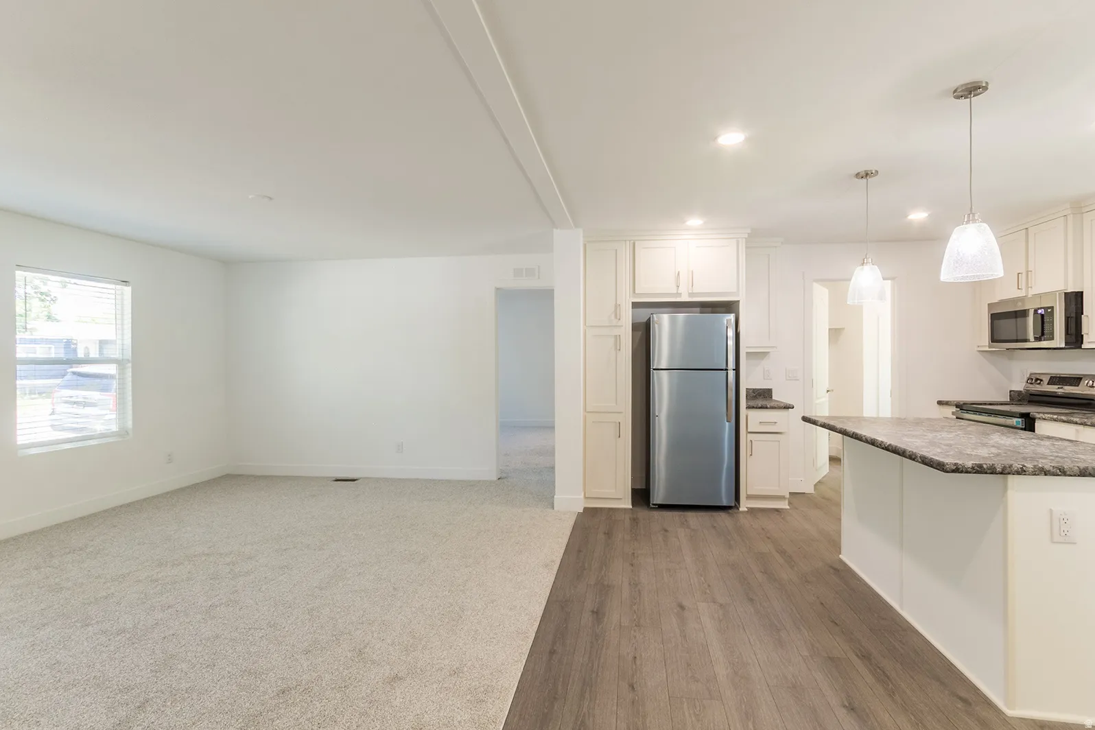 Open-concept kitchen and living area featuring wood-finish flooring, recessed lighting, white cabinetry, stainless steel appliances, and a kitchen island with seating