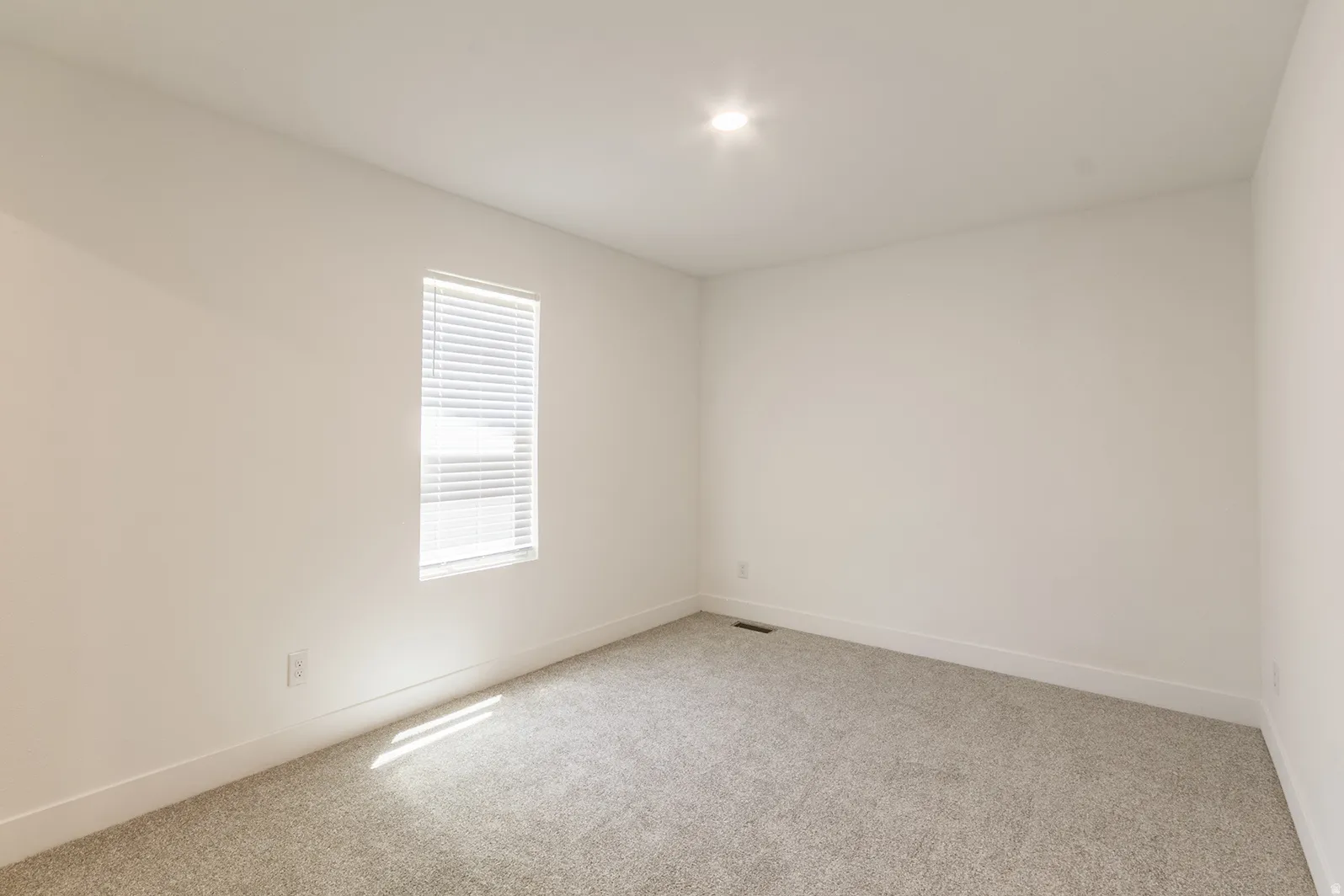 Neutral wall paint with carpet flooring, a single window with blinds, and recessed ceiling lighting