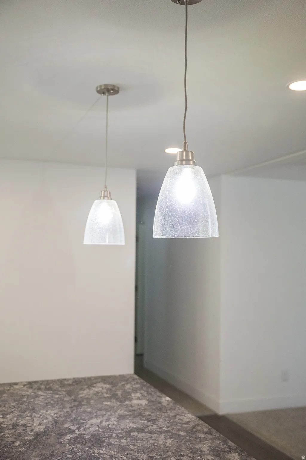 Two pendant lights with brushed nickel hardware illuminate a textured countertop