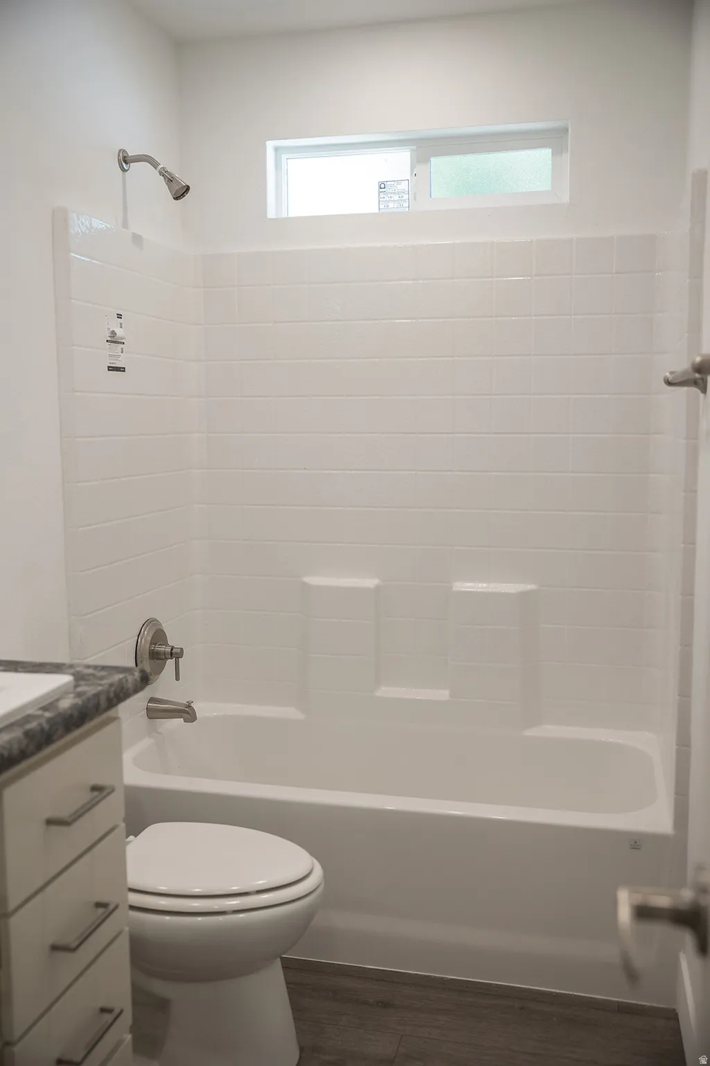 White subway tile shower surround with integrated soap dishes, brushed nickel fixtures, a sliding transom window, and wood-finish flooring