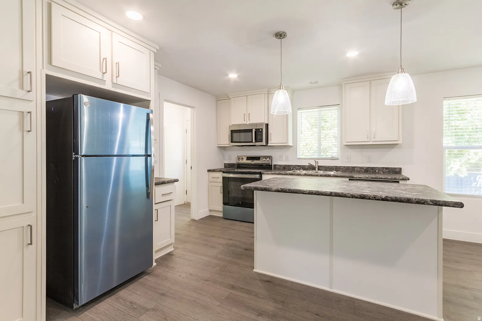 Kitchen featuring an island with stone-finish countertops, white cabinetry, stainless steel appliances, and pendant lighting