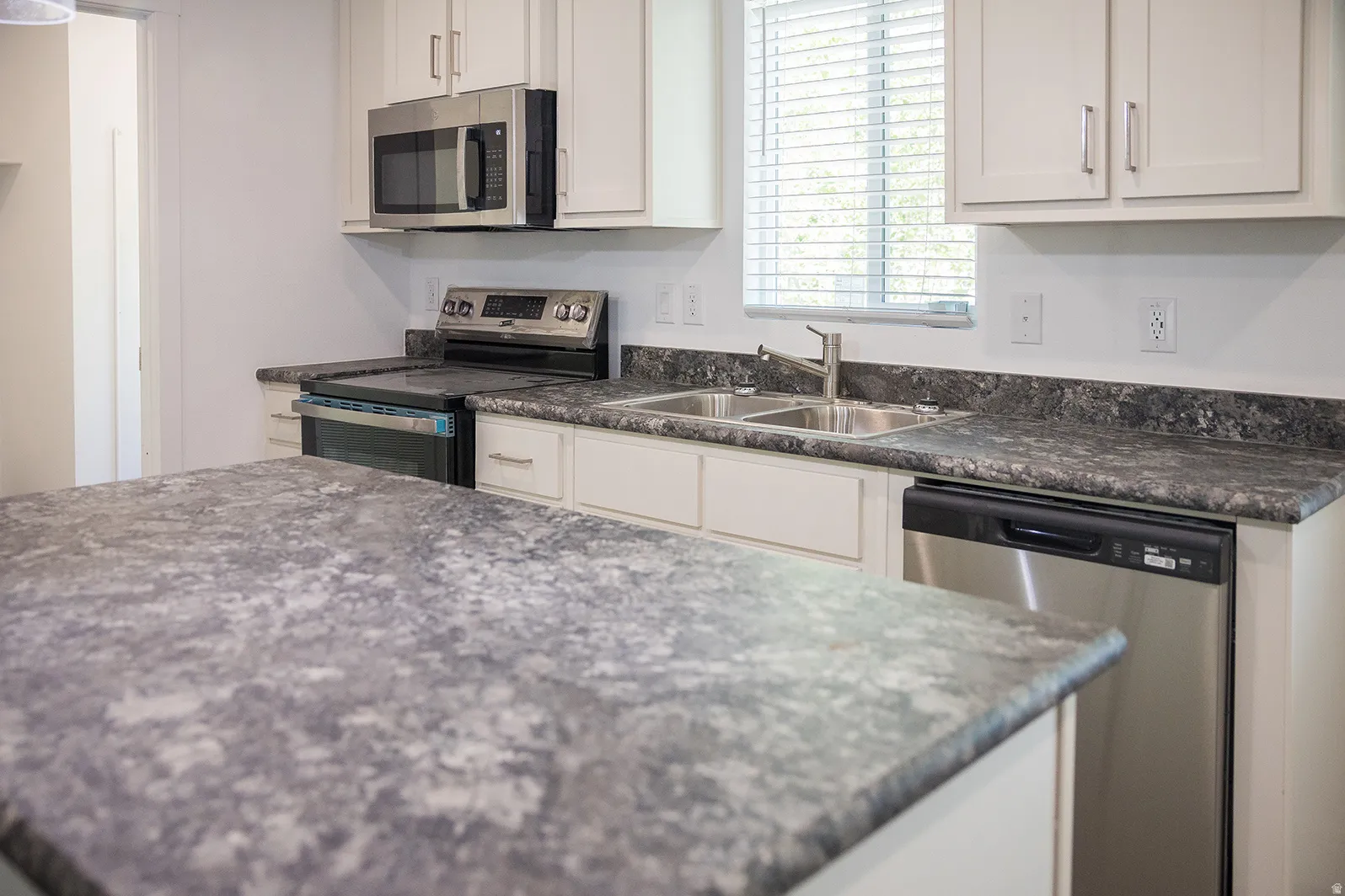 Kitchen featuring light cabinetry, a patterned countertop, and stainless steel appliances