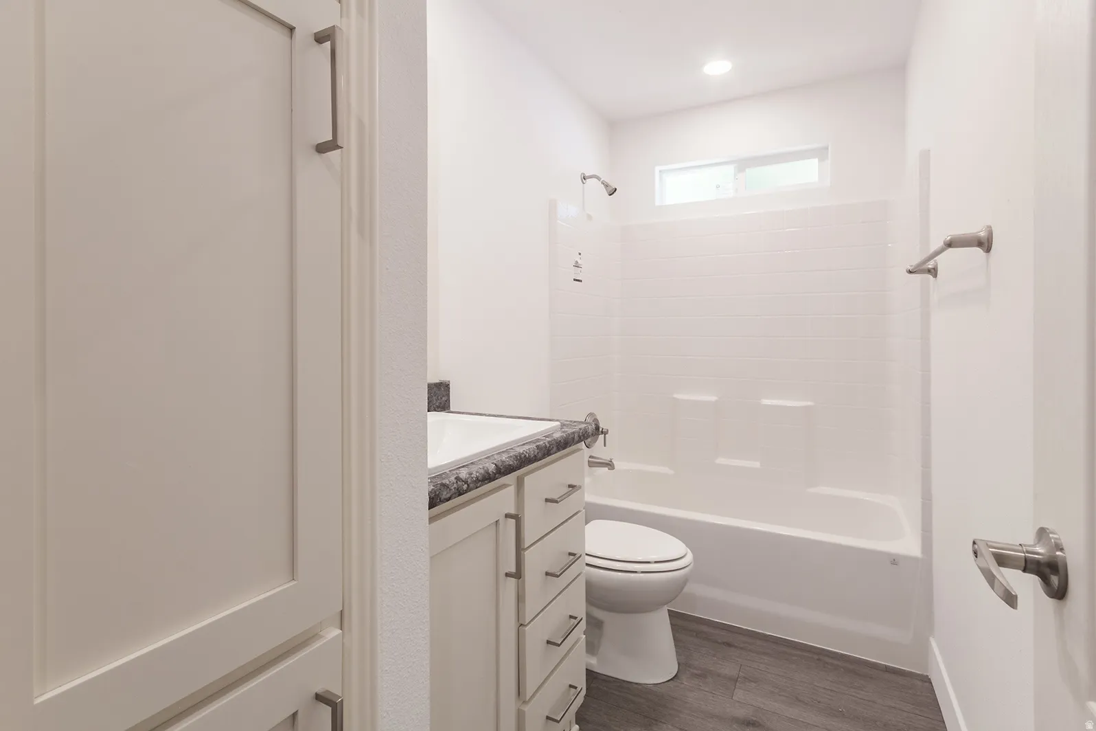Bathroom featuring a white bathtub with subway tile surround, dark wood-finish flooring, a white vanity with dark countertop, and recessed lighting