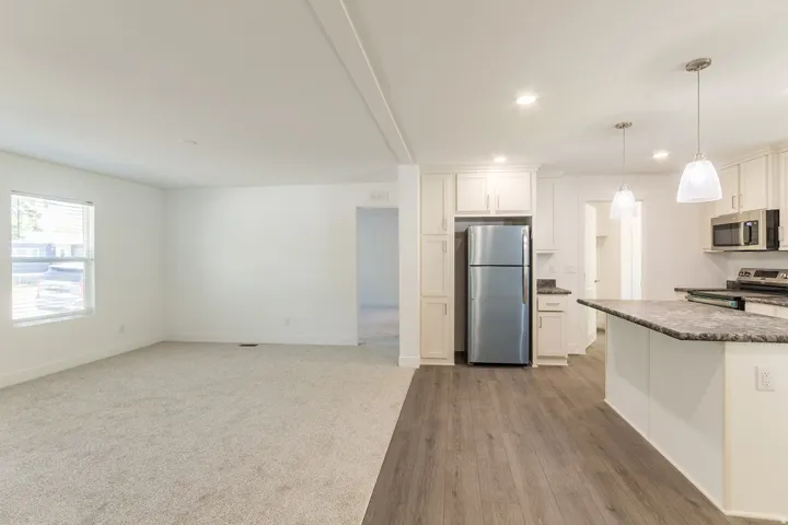 Open-concept kitchen and living area featuring wood-finish flooring, recessed lighting, white cabinetry, stainless steel appliances, and a kitchen island with seating