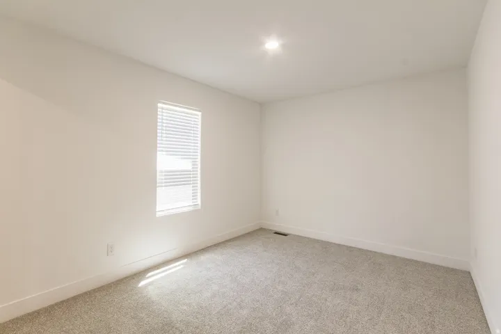 Neutral wall paint with carpet flooring, a single window with blinds, and recessed ceiling lighting