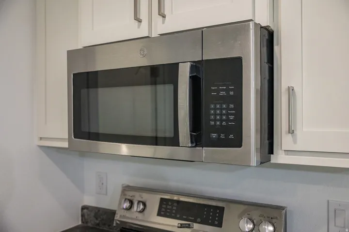 Stainless steel over-the-range microwave with white shaker-style cabinetry, dark speckled countertop, and stainless steel range