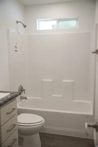 White subway tile shower surround with integrated soap dishes, brushed nickel fixtures, a sliding transom window, and wood-finish flooring