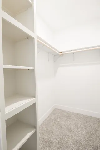 Walk-in closet featuring built-in shelving, white walls, light gray carpet, white baseboards, and a garment rod with wire shelving
