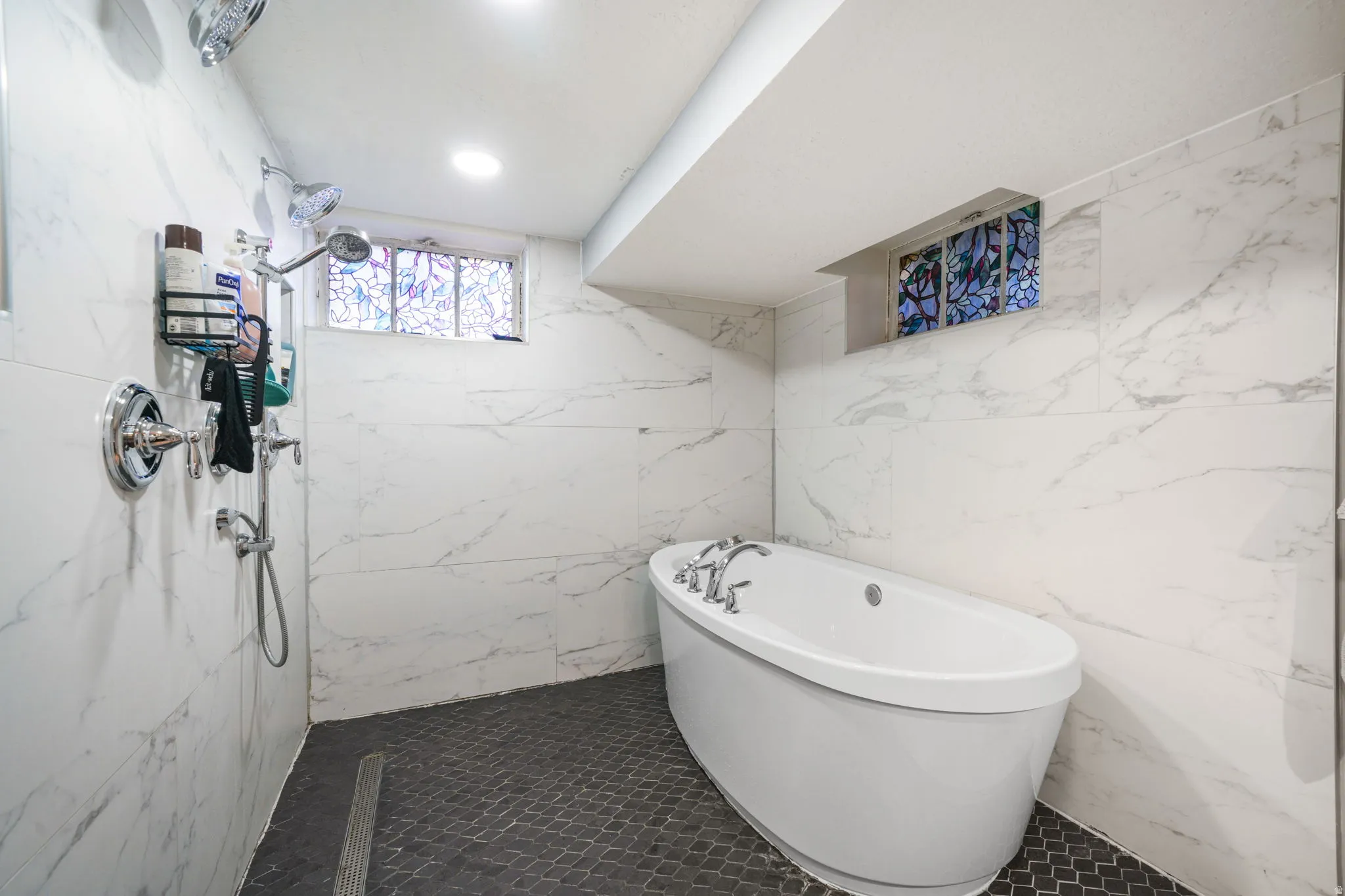 Freestanding soaking tub with chrome fixtures, surrounded by white marble-look tile walls