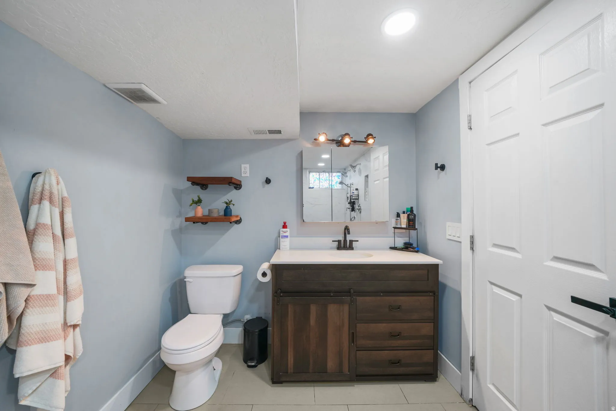 Modern bathroom featuring a wood-finish vanity with a light-colored countertop and dark bronze fixtures