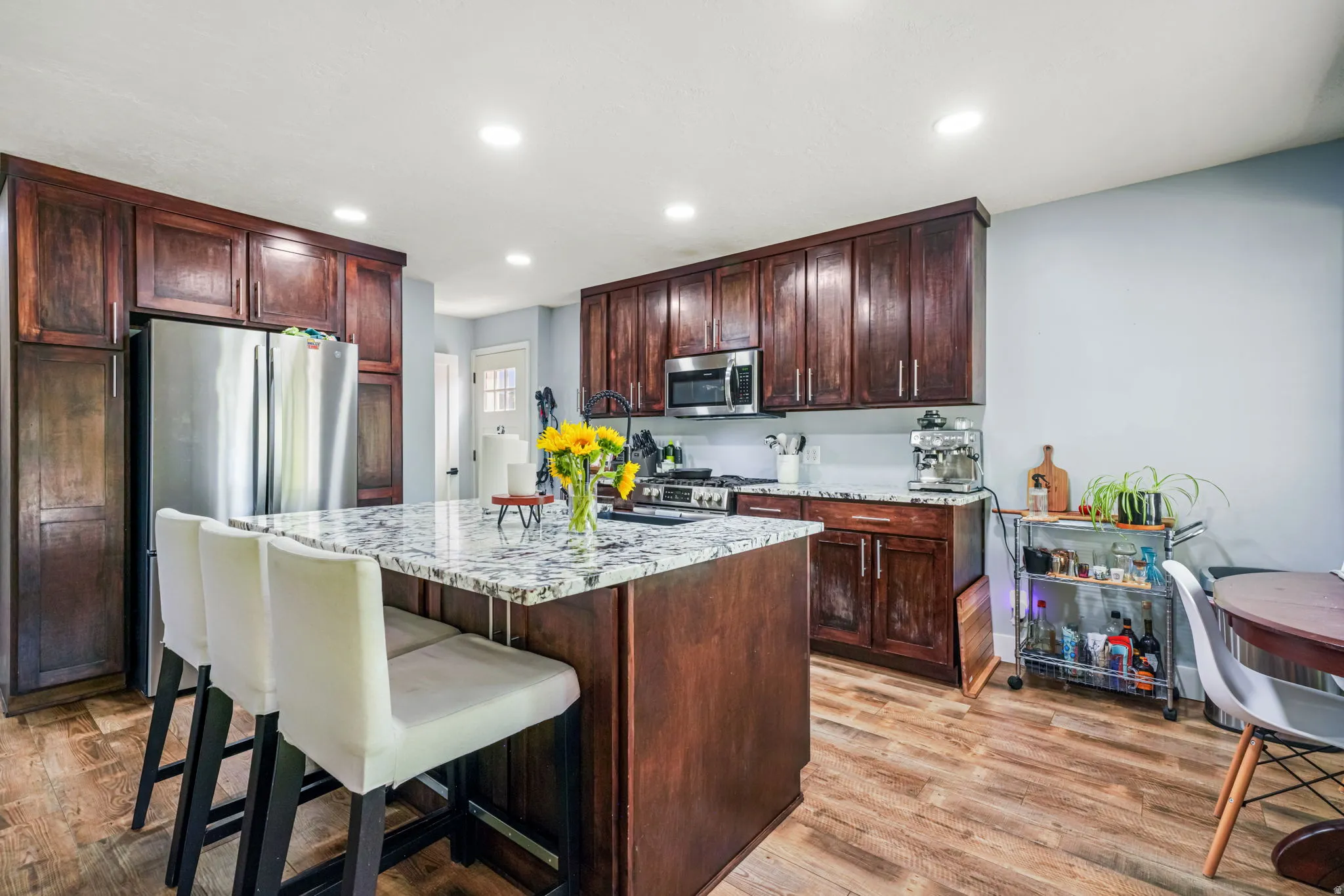 Kitchen featuring a central island with a stone countertop, dark wood-finish cabinetry, stainless steel appliances, recessed ceiling lighting, and wood-finish flooring