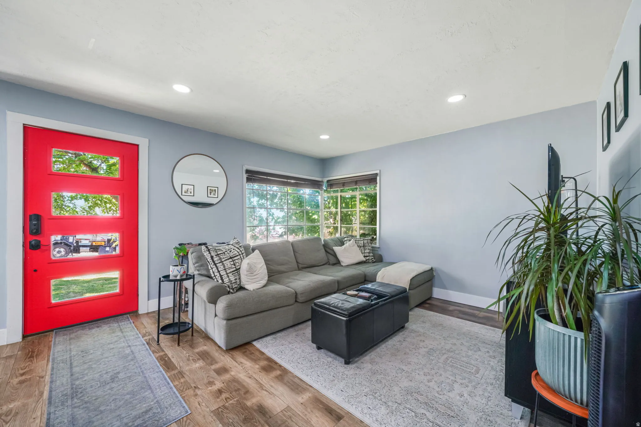 Vibrant red entry door with multiple glass panes, wood-finish flooring, recessed lighting, and a large window with white trim