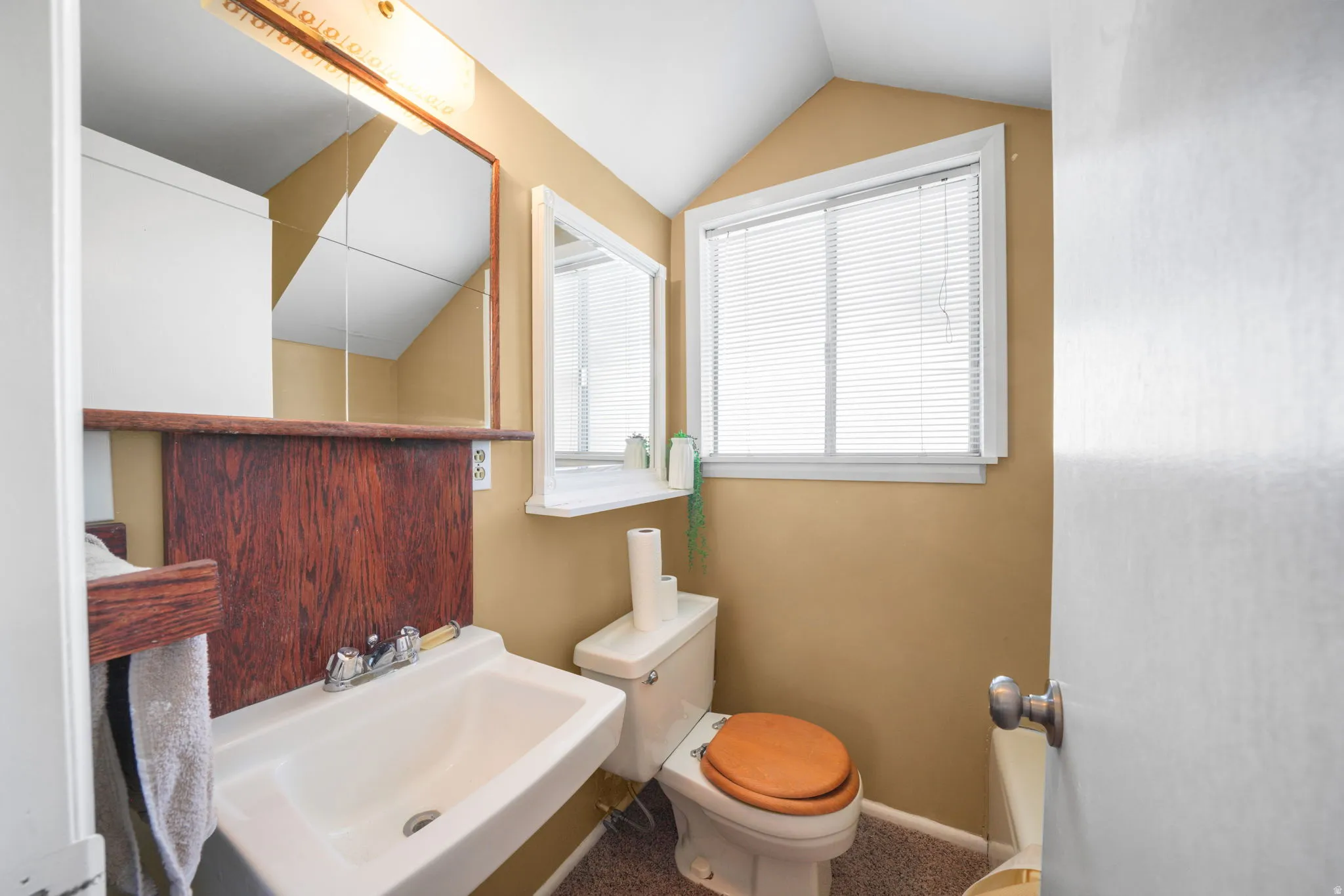 Bathroom featuring a wall-mounted sink with chrome faucet, a toilet with a wood-finish seat, a mirrored medicine cabinet, and an additional wall-mounted mirror
