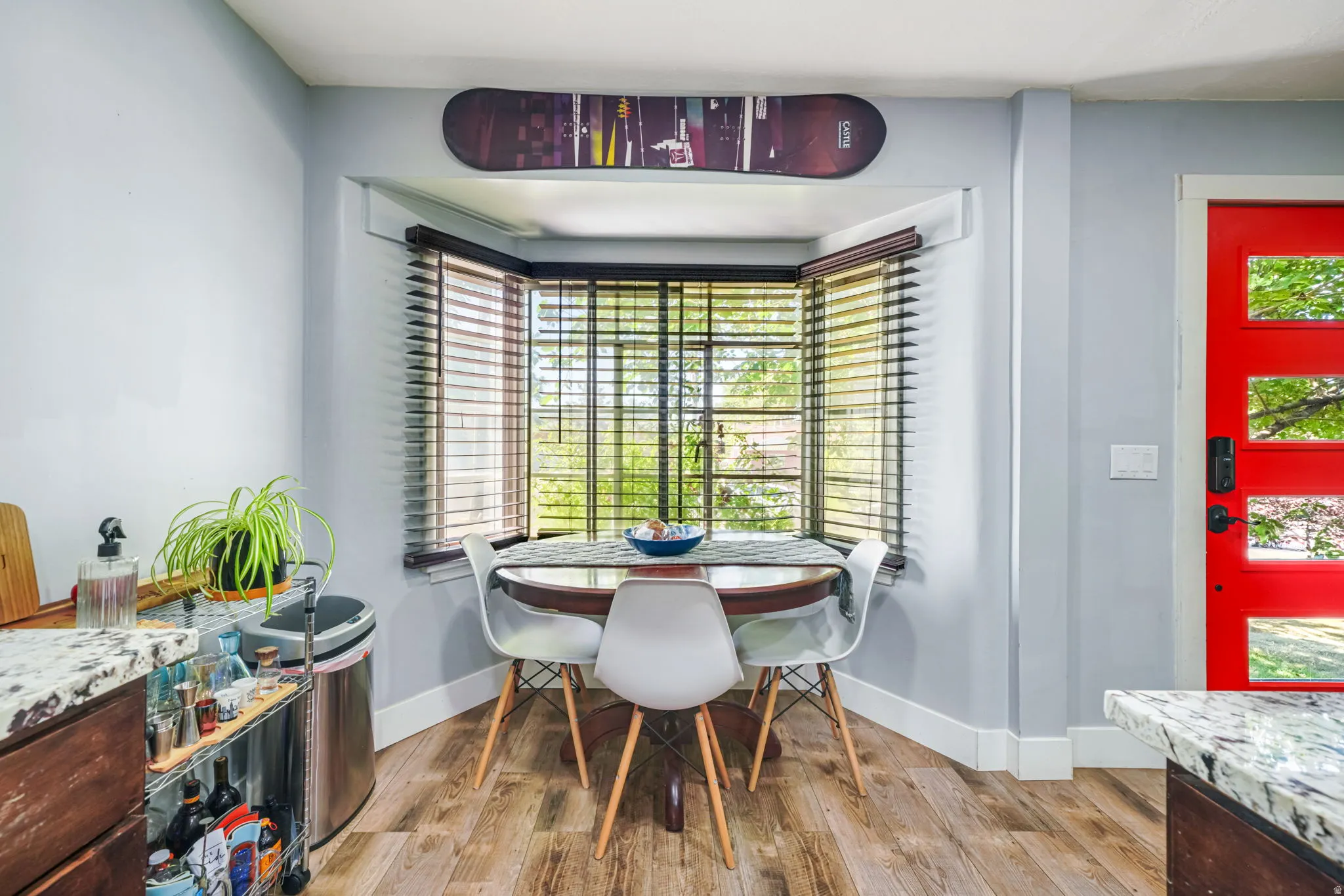 Light-filled dining nook featuring a bay window with natural light, wood-finish flooring, and a bold red entry door with multiple glass panes