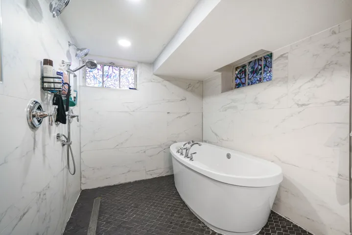 Freestanding soaking tub with chrome fixtures, surrounded by white marble-look tile walls