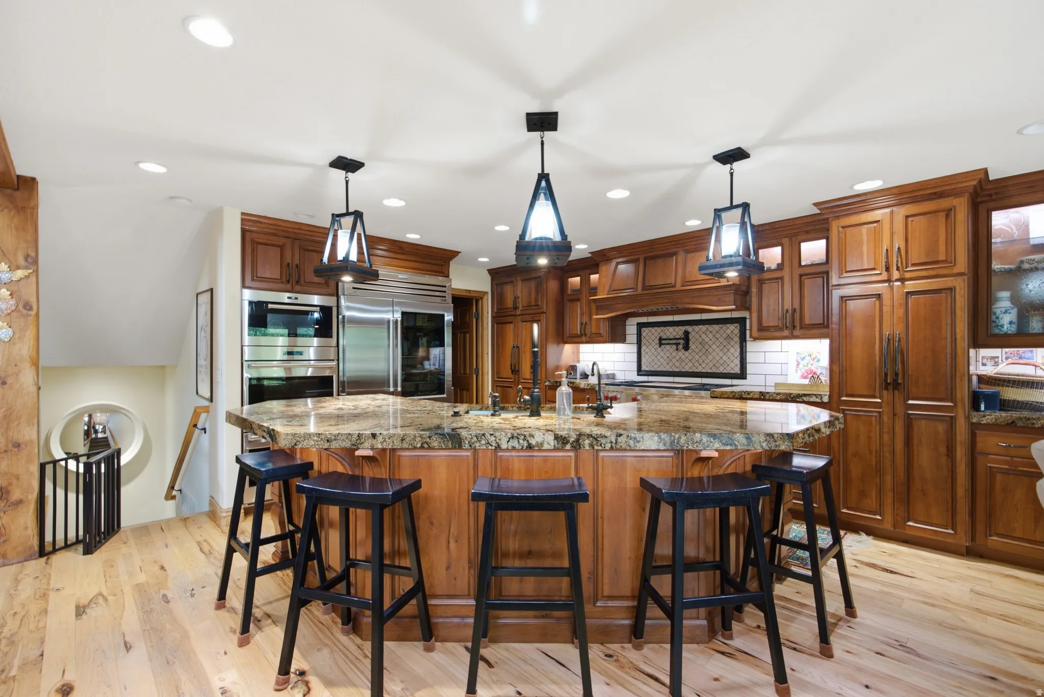 Gourmet kitchen featuring a large curved island with a stone countertop, custom wood cabinetry, stainless steel appliances, and wood-finish flooring