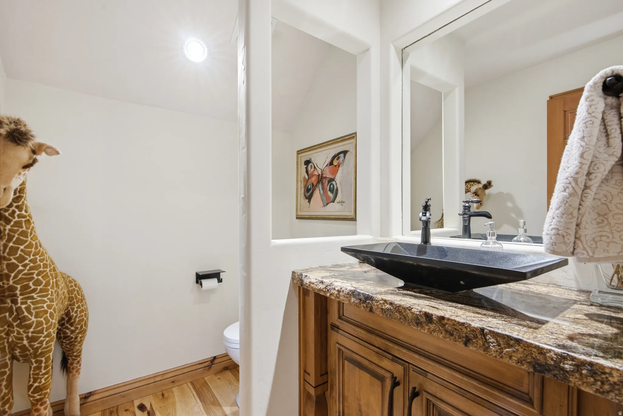 Bathroom vanity featuring a vessel sink with a black faucet, stone countertop, wood cabinetry, and a framed mirror