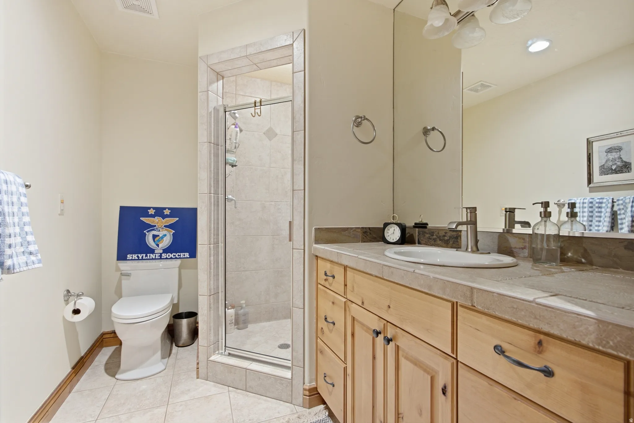 Bathroom featuring a light wood-finish vanity with an undermount sink, tiled countertop, and an expansive mirror